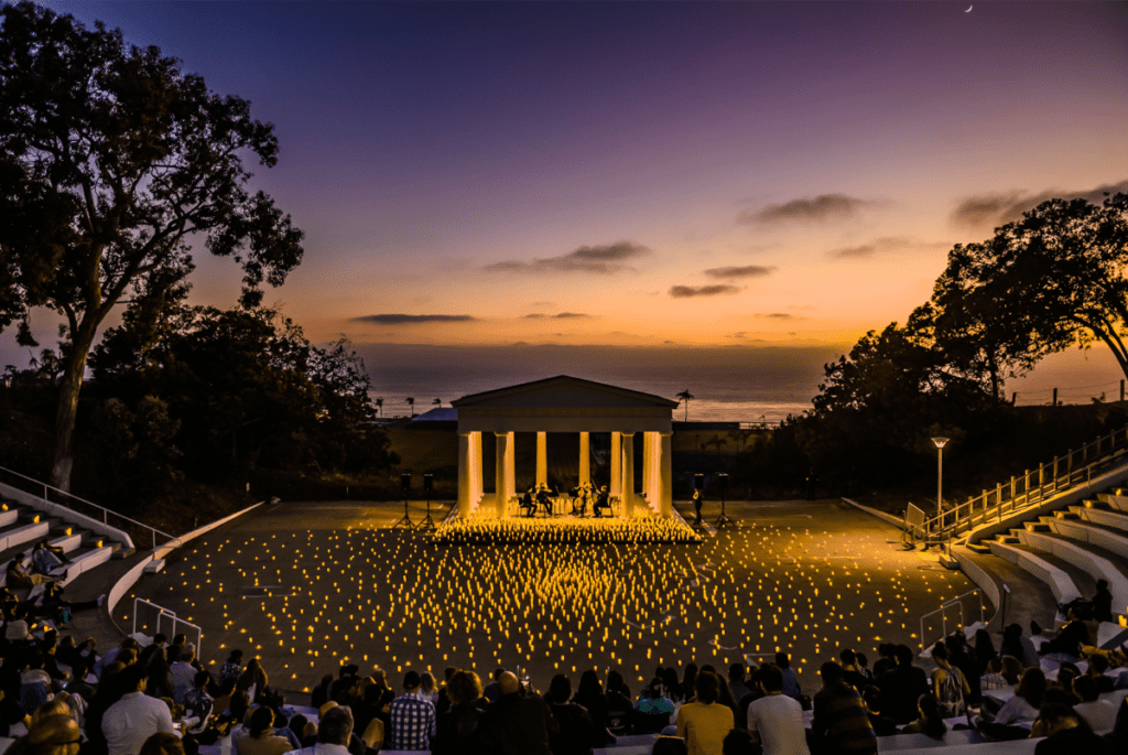 A wide shot of The Greek Amphitheater venue in San Diego taken from the audience watching a string quartet perform on the Greek-style stage with the setting covered entirely by candles.