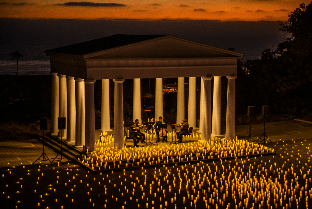 A string quartet performing on a candlelit stage covered by a Greek-style open-air building held by columns at the Greek Amphitheater in San Diego.