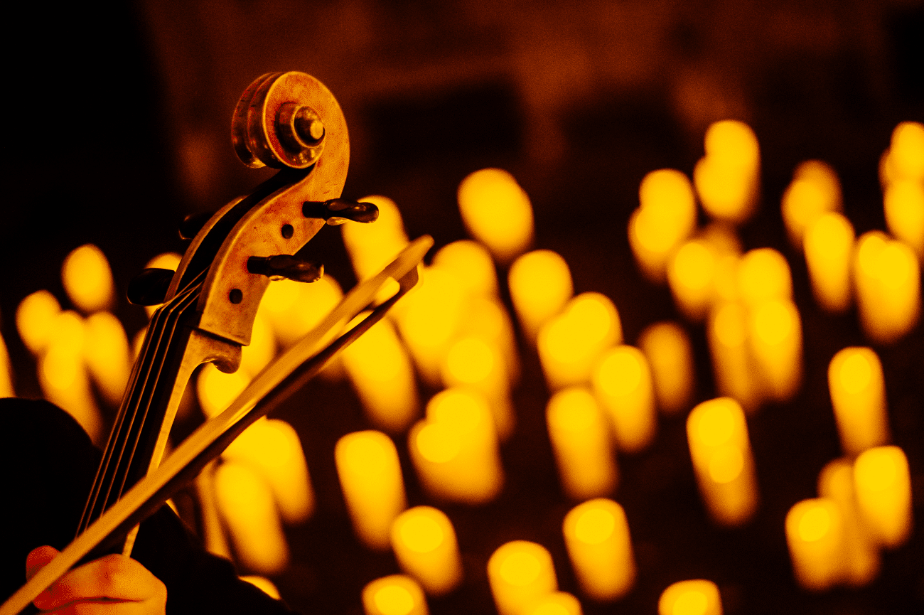 The top of a violin and bow with the glow of candlelight in the background.