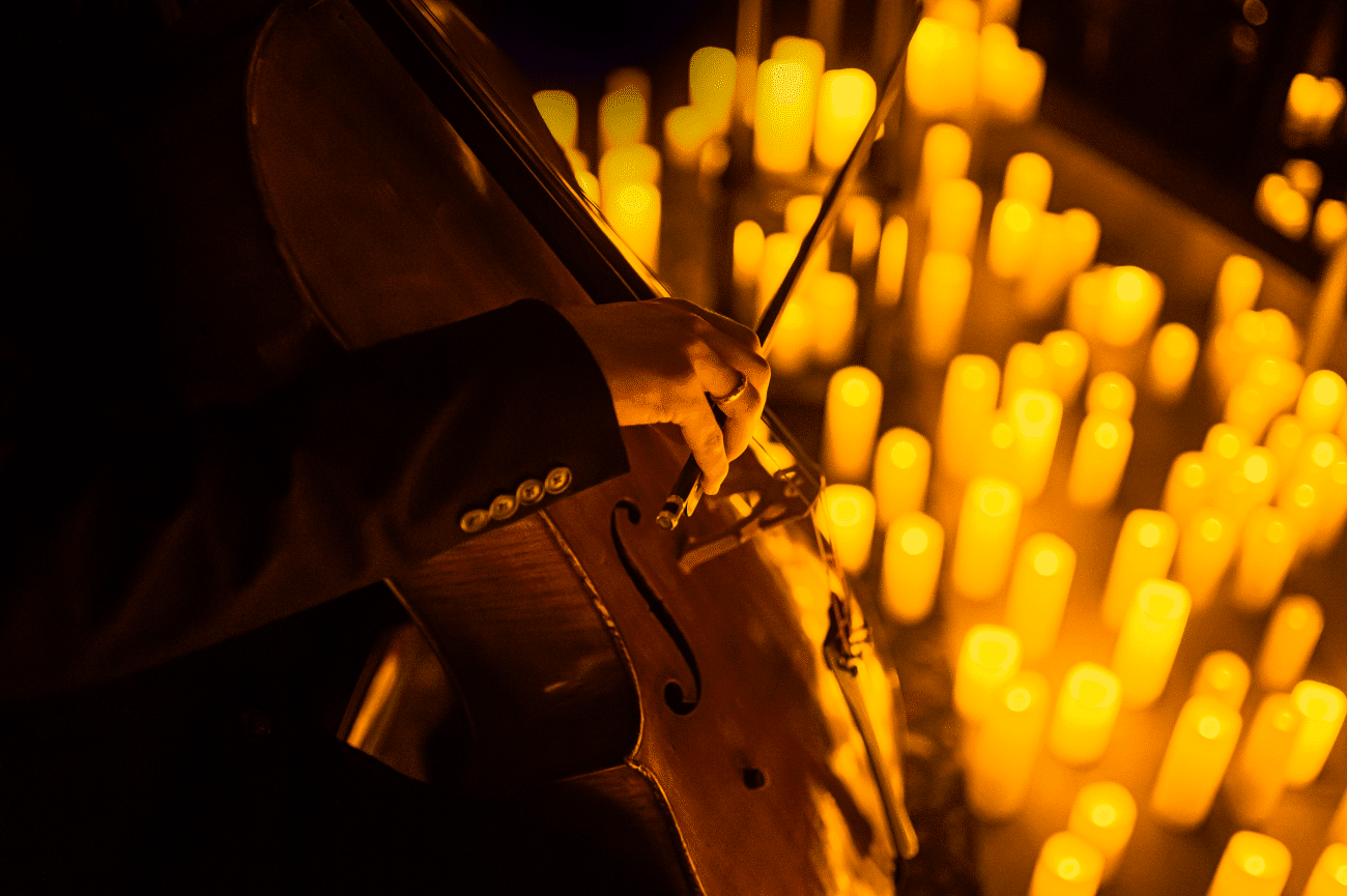 A man playing the cello surrounded by candlelight.
