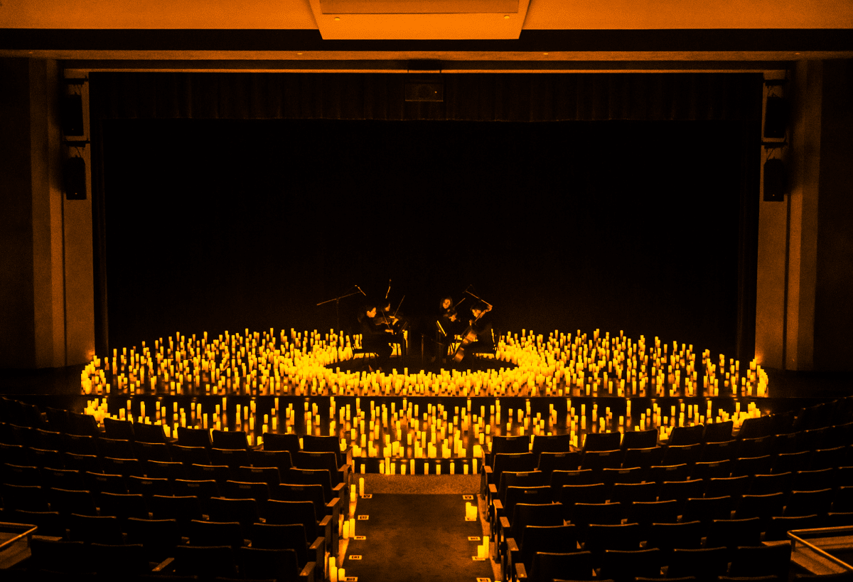 A string quartet perfomring on a stage surrounded by a sea of candles.