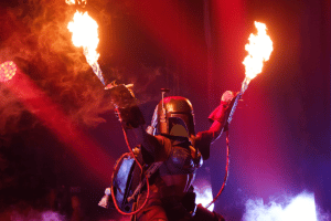 Boba Fett the Star Wars character holds flame throwers onstage