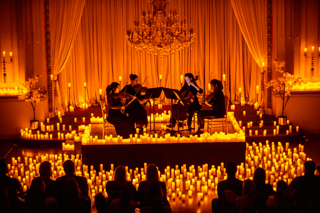 A string quartet performs on stage surrounded by candles