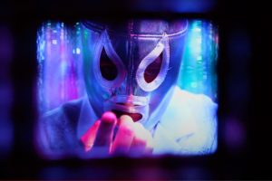 A masked wrestler reaches towards the camera