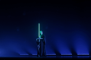 A woman dressed as a Jedi holds a lightsaber