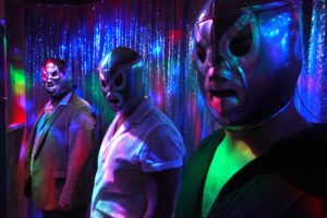 Three luchadores look at the camera wearing masks