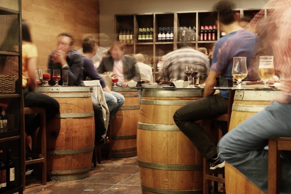 A wine bar setting with people sitting up at barrel tables.